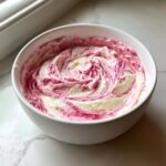 A white bowl filled with creamy, swirled strawberry cheesecake dip showing streaks of pink and white.