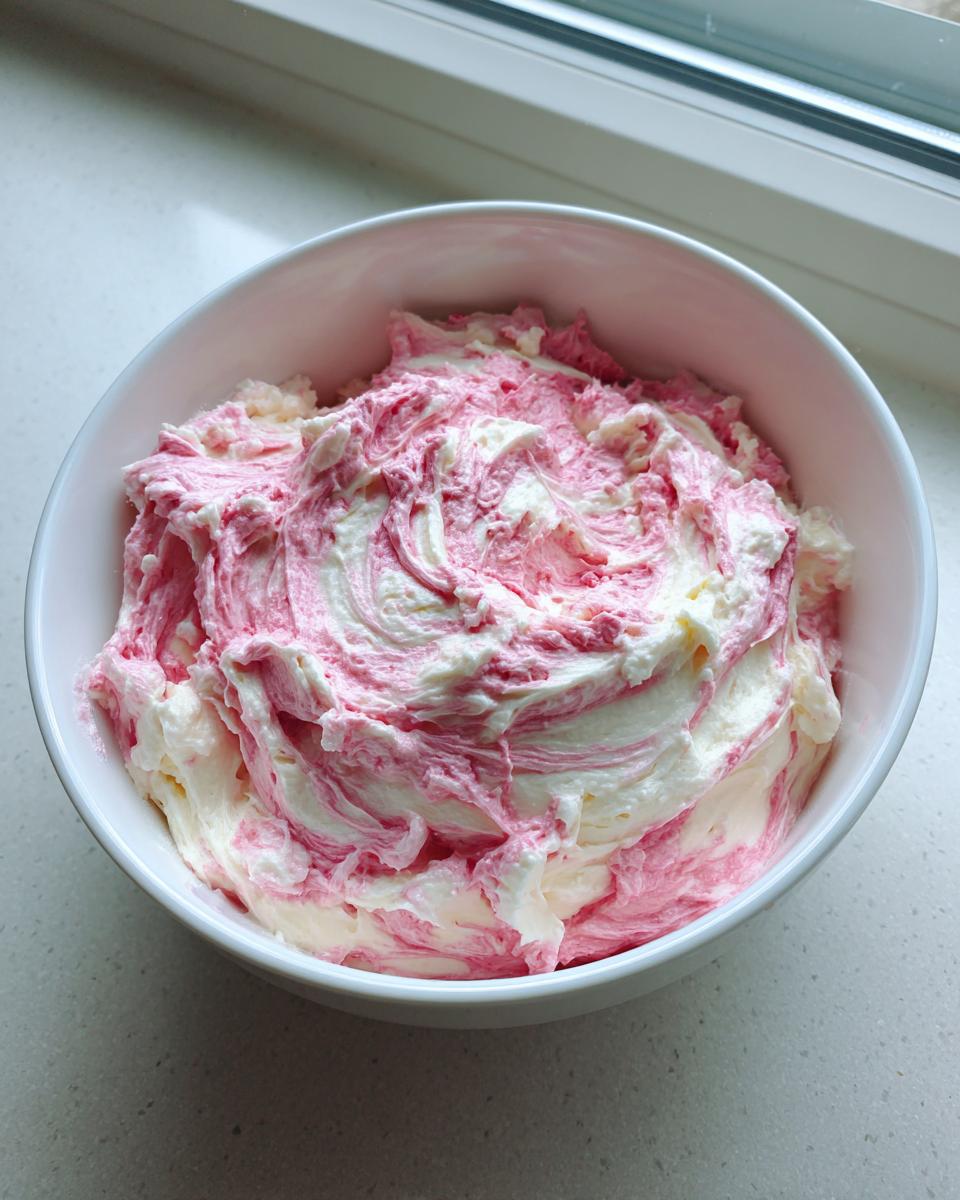 A white bowl filled with freshly mixed strawberry cheesecake dip, showing swirls of pink and white cream cheese mixture.