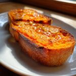 Two slices of bright orange sweet potato toast topped with glistening honey, sitting on a white plate.
