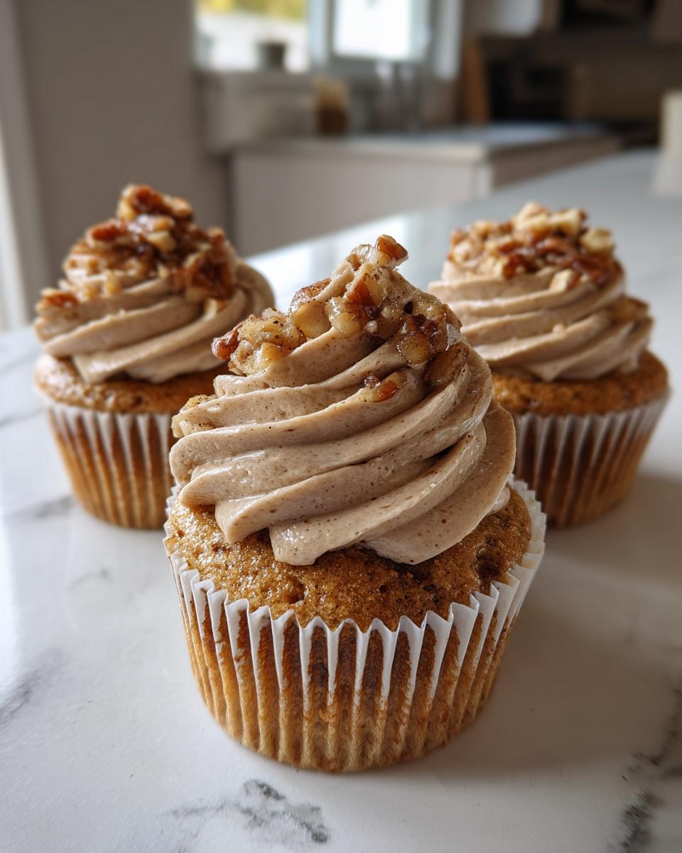 Three delicious pecan pie cupcakes topped with swirled, spiced frosting and candied pecans.
