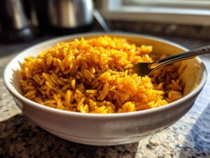 A close-up of a white bowl filled with vibrant, fluffy turmeric rice, with a fork resting inside.