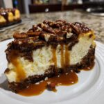 Close-up of a rich slice of turtle cheesecake featuring a creamy center, dark crust, topped with pecans, chocolate, and dripping caramel sauce.