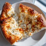 Close-up of a thick slice of ultimate white pizza topped generously with creamy ricotta and herbs.