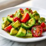 Close-up of a fresh avocado salad featuring diced avocado, halved cherry tomatoes, and cucumber chunks tossed in a light dressing.