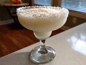 A frosty white Christmas margarita in a glass with a thick rim of shredded coconut.