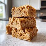 A stack of three chewy, golden-brown cheerio bars made with cereal and a sticky binder.
