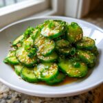 Close-up of vibrant green slices of asian cucumber salad tossed in a savory dressing and topped with sesame seeds.