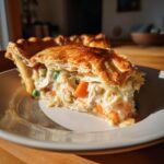 Close-up of a thick slice of chicken pot pie recipe filling with carrots and peas, topped by a golden, flaky crust.