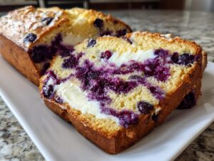 A thick slice of moist Blueberry Cream Cheese Bread showing vibrant purple blueberry swirls and a rich cream cheese center.