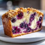 Close-up of a moist slice of Blueberry Cream Cheese Bread showing swirls of cream cheese and bursting blueberries.