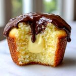 Close-up of a Boston cream pie cupcakes cut in half showing vanilla cream filling and chocolate ganache topping.