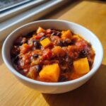 Close-up of a white bowl filled with rich, tomato-based butternut squash chili and black beans.