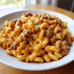 A close-up shot of a white bowl filled with creamy, cheesy taco pasta mixed with seasoned ground beef.