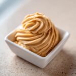 A beautiful swirl of creamy, light brown cinnamon butter piped into a small white square dish.
