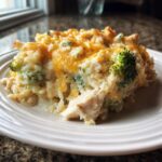 A close-up serving of creamy chicken and broccoli rice casserole topped with melted cheddar cheese.