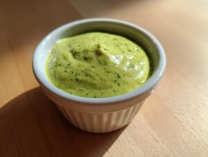 A small white ramekin filled with bright green, creamy cilantro lime sauce, sitting on a wooden surface.