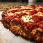 Close-up of a baked cauliflower pizza crust topped with bright red sauce and melted white mozzarella cheese.