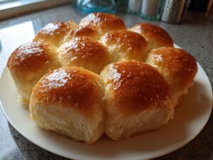 A cluster of eight soft, fluffy dinner rolls with a shiny, buttery glaze on a white plate.