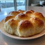 A cluster of freshly baked, golden brown dinner rolls with a shiny glaze, served on a white plate.