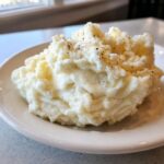 A generous serving of creamy, fluffy mashed potatoes sprinkled with cracked black pepper on a white plate.