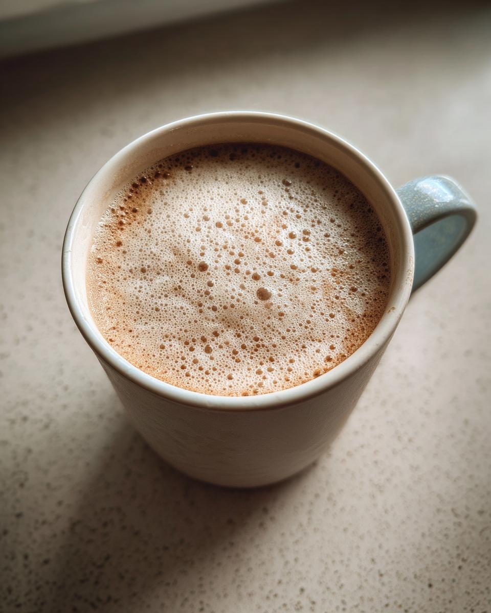 Close-up of a creamy, foamy white hot chocolate in a light-colored mug.