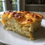 A thick, square slice of french onion potato bake with layers of tender potatoes and a golden, cheesy crust.