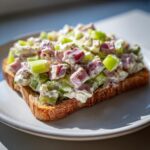 Close-up of creamy ham salad recipe with diced ham and celery piled high on a slice of toasted bread.
