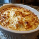 Close-up of a baked hot crab dip recipe in a white oval dish, featuring a bubbly, golden-brown cheesy top.
