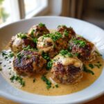 Close-up of six juicy swedish meatballs smothered in creamy brown gravy and topped with fresh parsley.