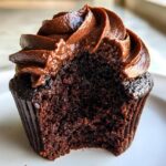 Close-up of a moist chocolate cupcake with rich chocolate frosting, showing a bite taken out.