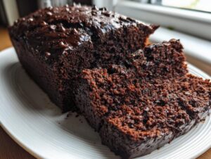A close-up of a rich, dark chocolate zucchini bread loaf, partially sliced, showing its moist texture and chocolate chip topping.