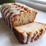 Close-up of moist eggnog bread loaf with one slice cut, drizzled generously with white eggnog glaze.