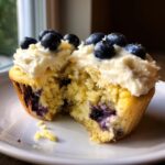 Close-up of a lemon blueberry cupcake with a bite taken out, showing moist crumb and fresh blueberries.