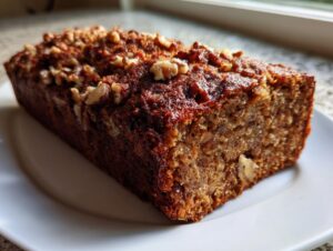 A close-up of a moist, dark brown persimmon bread loaf topped with chopped walnuts, resting on a white plate.