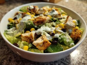 Close-up of a vibrant southwest salad featuring grilled chicken, corn, black beans, and a creamy cilantro dressing.