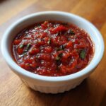Close-up of rich, chunky tomato sauce seasoned with fresh green herbs in a small white bowl.