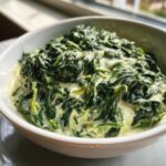 Close-up of rich, dark green creamed spinach served in a white bowl, highlighting the creamy sauce.