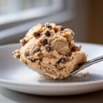 A close-up of a spoonful of edible chocolate chip cookie dough recipe, ready to eat.