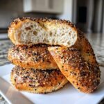 Close-up of stacked sourdough discard bagels, one cut open showing the airy interior and everything bagel seasoning.