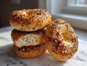 A stack of three everything sourdough discard bagels, one broken open to show the fluffy interior.