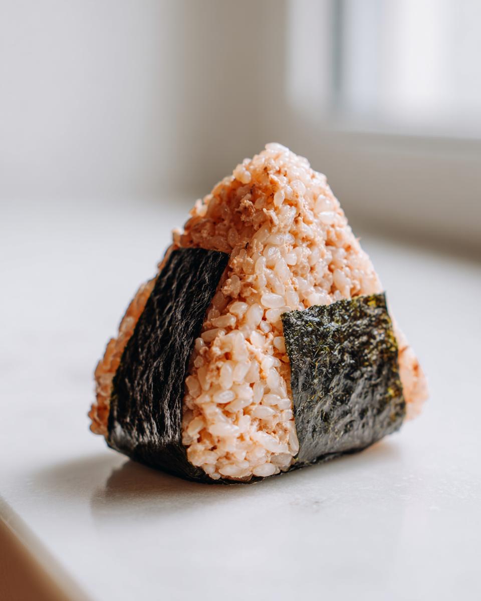 Close-up of a triangular tuna onigiri rice ball wrapped with a strip of dark nori seaweed.