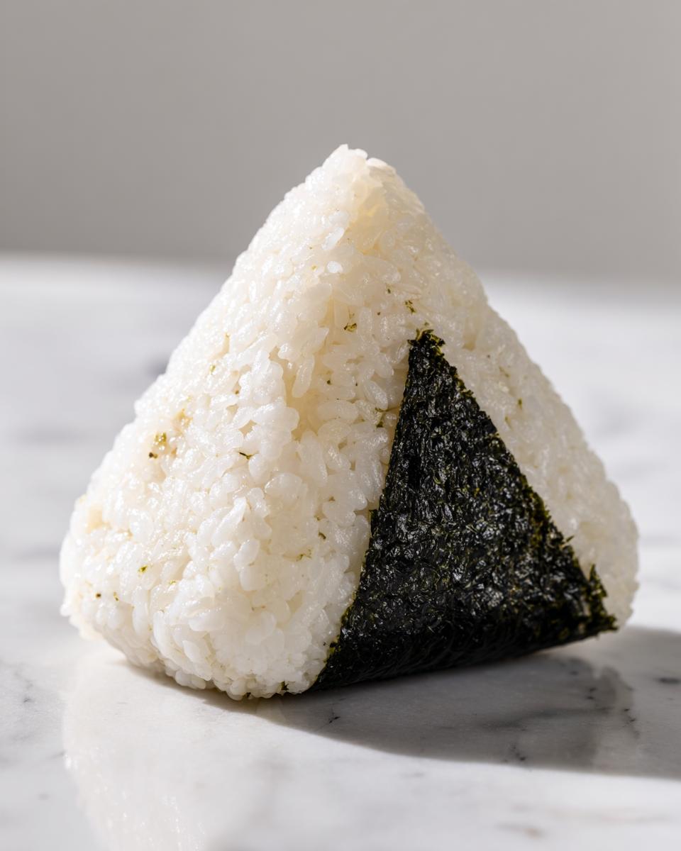 A close-up of a classic triangular tuna onigiri made with white rice and wrapped with a piece of dark nori seaweed.