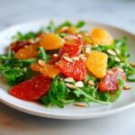 Close-up of a bright citrus salad featuring ruby red grapefruit, orange segments, arugula, and slivered almonds.