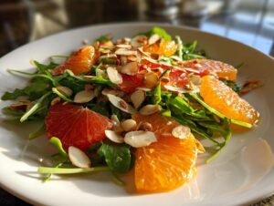 Close-up of a vibrant citrus salad featuring bright orange and red grapefruit segments over arugula, topped with slivered almonds.