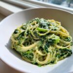 A close-up of creamy spinach pasta tossed in a white bowl, topped with grated cheese.