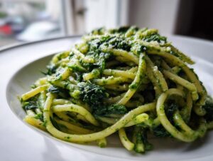 Close-up of creamy spinach pasta tossed in a vibrant green sauce, served on a white plate.