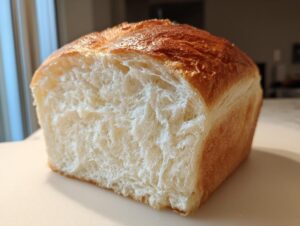 Close-up of a freshly baked loaf of milk bread cut in half, showing its incredibly soft, white, and fluffy interior crumb.