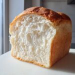 A loaf of homemade milk bread cut in half, showing its incredibly soft, white, and fluffy interior crumb structure.