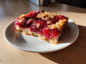 A close-up of a square slice of bright red cherry dump cake with a crumbly topping on a white plate.