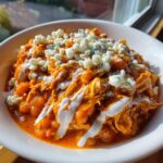 Close-up of a bowl of vibrant orange slow cooker buffalo chicken chili topped with blue cheese crumbles and a drizzle of ranch.